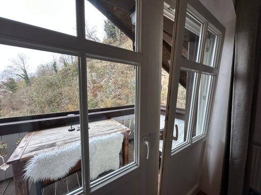 Ein Blick auf einen Balkon mit einem Holztisch und Aussicht auf grüne Bäume.