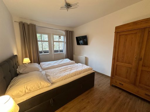 Helles Schlafzimmer mit zwei Einzelbetten, einem Holzschrank und Fernseher.