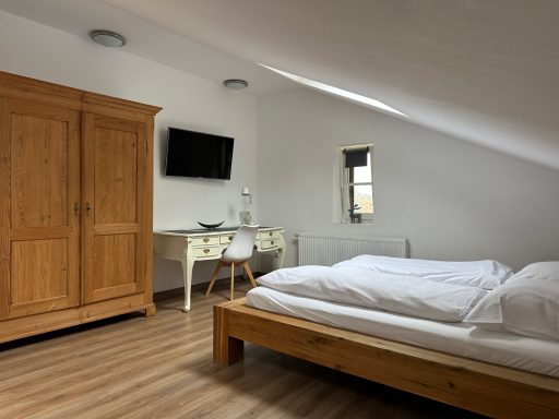 Helles Schlafzimmer mit einem Doppelbett, Schreibtisch und einem großen Holzschrank.
