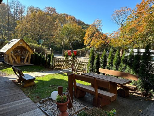 Gemütlicher Garten mit Holzsitzgelegenheiten und herbstlichen Bäumen im Hintergrund.