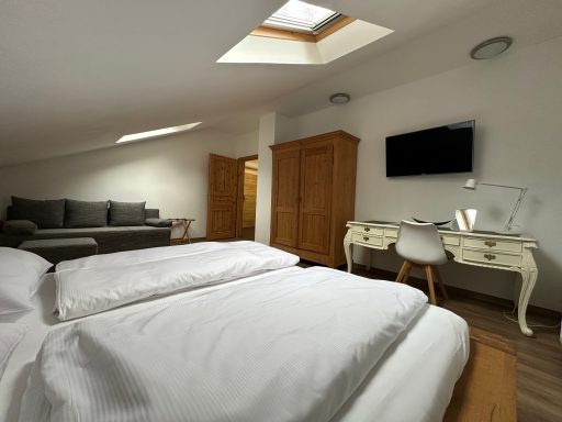 Helles Dachzimmer mit zwei Betten, Couch, Arbeitsbereich und Holzschrank.